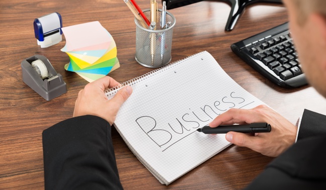 A businessman with a notebook, sitting at a desk with a corner of a keyboard visible. 