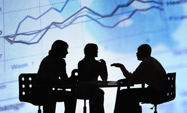A silhouette of 3 people in a business meeting with an upward graph in the background. 