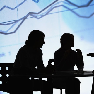 A silhouette of 3 people in a business meeting with an upward graph in the background. 