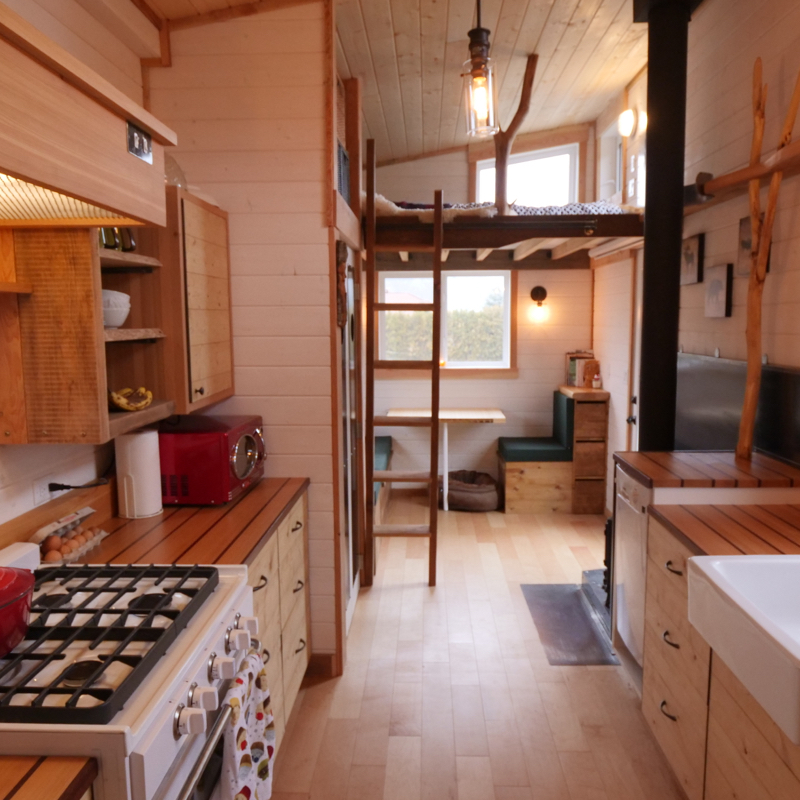 Shown is the interior of a tiny house, showing the kitchen in the foreground with lots of wood everywhere.