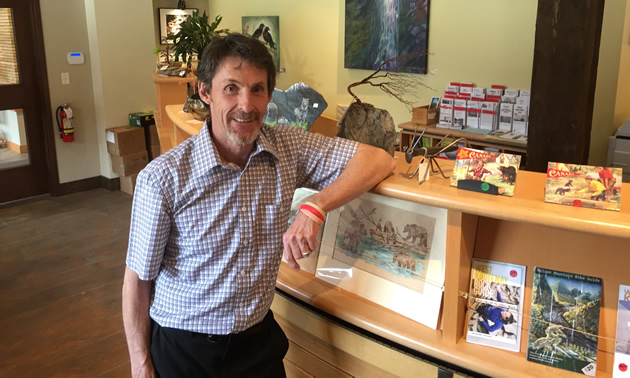 Tom Thomson leans against a desk in the Nelson & District Chamber of Commerce.