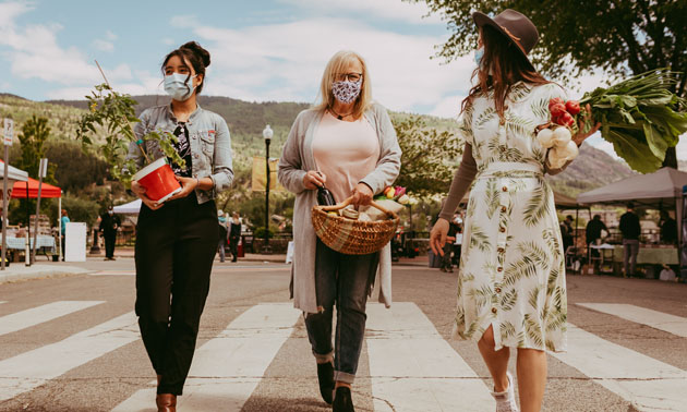 Three women walk through a farmers market. 