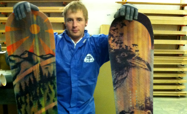 Greg in blue holds two snowboards with mountain and animal graphics.