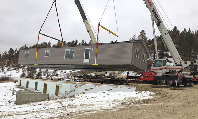 Large crane removing a mobile home from plot of land. 