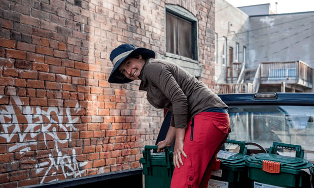Ashley Taylor is leaning over a green bin that she collects food waste in.