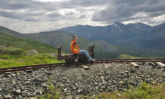 Terwoot sitting on small track equipment on train track, mountains in background. 