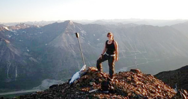 Terwoort standing on pile of rocks, mountain vista behind her. 