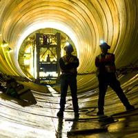 Two workers are silhouetted against a yellow lit tunnel. 