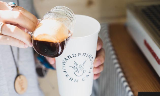 Coffee being poured from glass mug into Wandering Fern cup. 