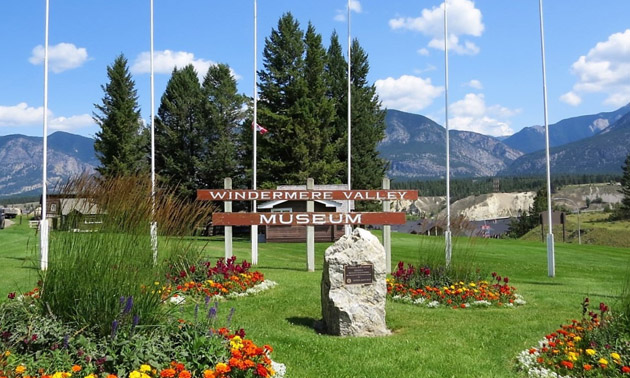 Windermere Valley Museum sign and neat beds of flowers, mountains in background. 