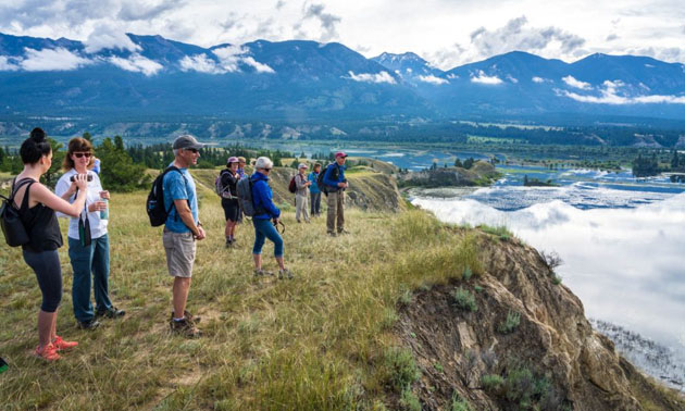 Bird watchers stand along a riverfront, mountains in background. 