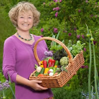 A women wears a pink cardigan and holds a basket overflowing with produce.