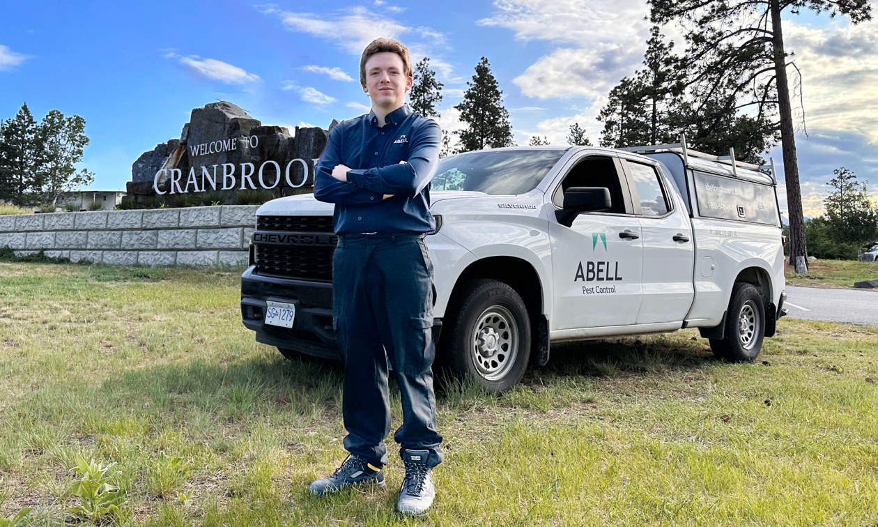 Pest control tech standing in front of the truck, parked by the Welcome to Cranbrook sign