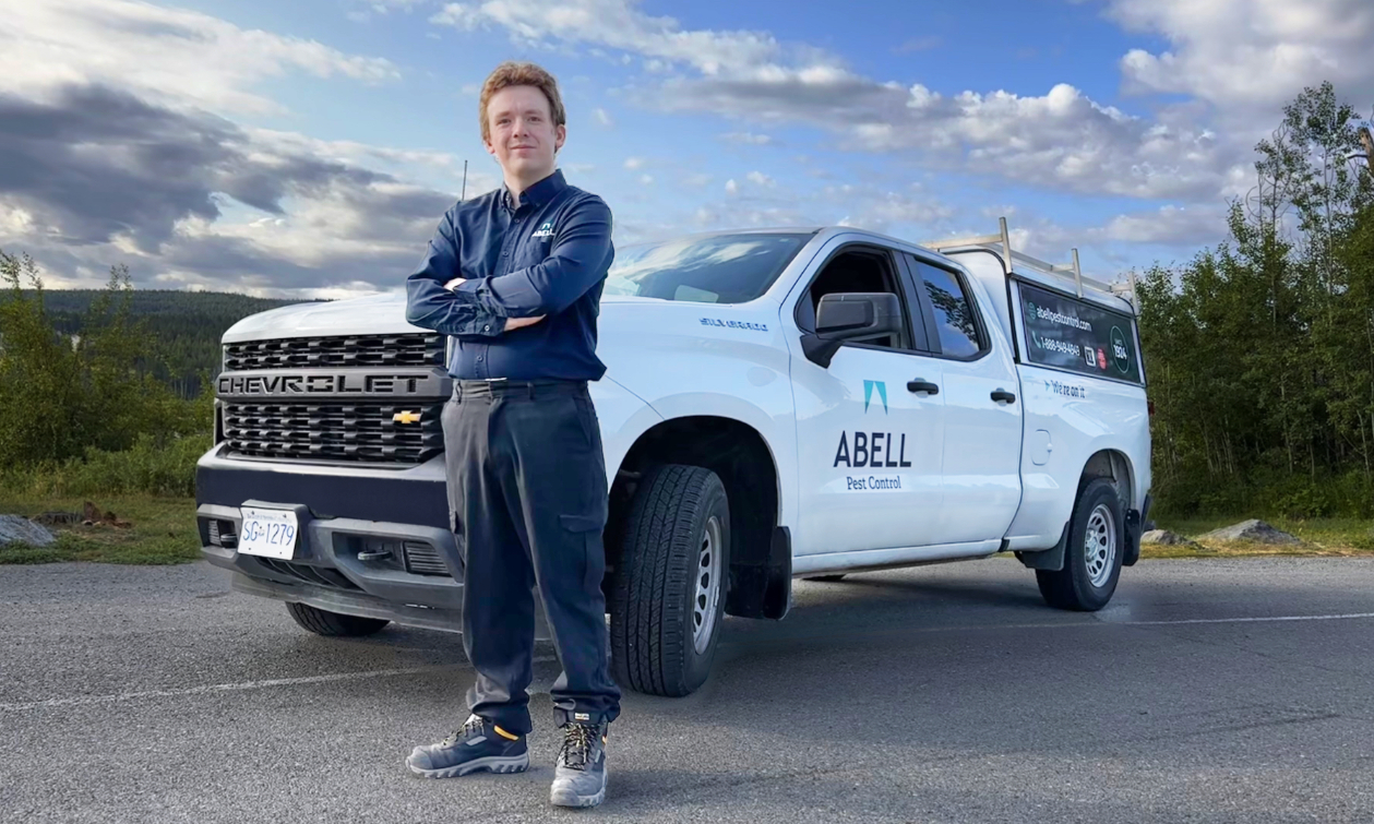 Pest control technician standing in front of a white company vehicle with Abell Pest Control on the side