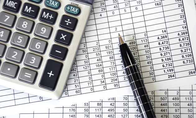 A photo of a calculator and a black pen on top of a spreadsheet. 