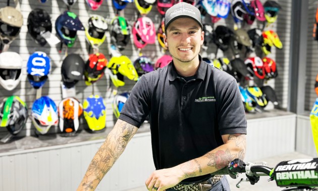 Dayton Pouliot with his arm on a bike handle with helmets in the background at All Seasons Motorsports