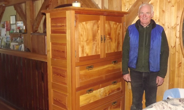 older man standing beside a finely crafted wooden cabinet