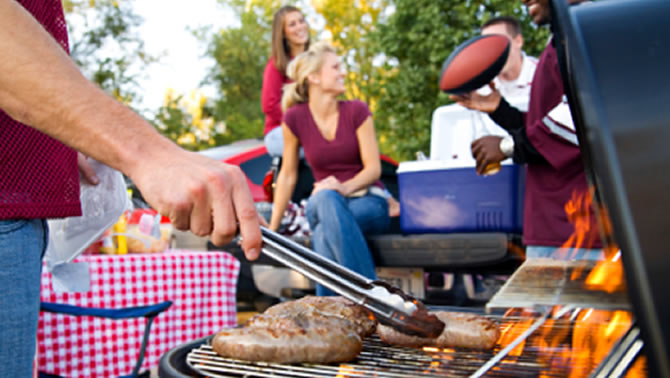 Close-up picture of food on BBQ, with people laughing in the background. 