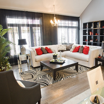 A living room with a white corner sofa, black book shelf and coffee table, and red cushions and accessories