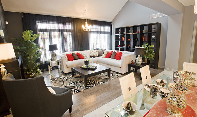 A living room with a white corner sofa, black book shelf and coffee table, and red cushions and accessories