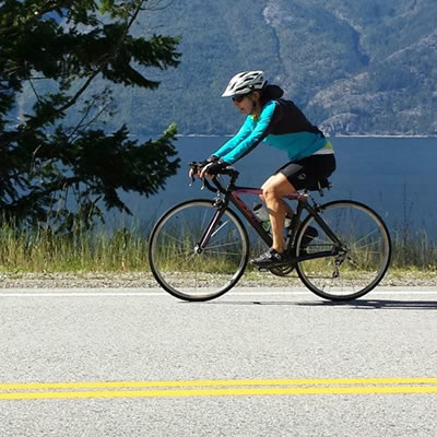 Picture of woman biking along a paved path beside a lake. 