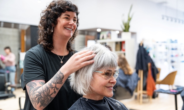 Dark haired stylist helping a lady with her hair, which is cut in a trendy bob