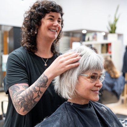 Dark haired stylist helping a lady with her hair, which is cut in a trendy bob