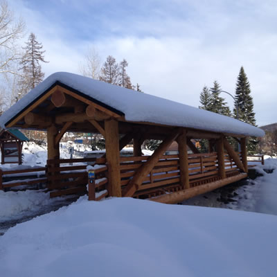 A covered log and timber pedestrian bridge is covered in snow.