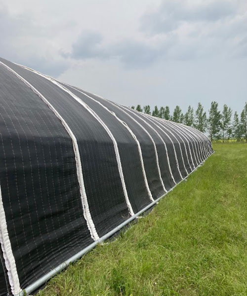 A large tunnel-style greenhouse with black cover over it. 