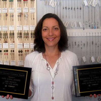 Custom jeweler Kara Clarke has won several chamber awards from the Kimberley Chamber of Commerce including Home Business of the Year. She stands in front of a wall full of hanging necklaces.