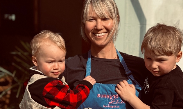 Chantel wearing a Burrito Grill apron and holding her two children