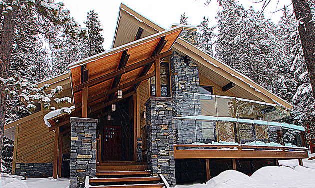 A Modern Mountain Alpine home design that includes a steep sloped roof, the combination of rock and wood work decoration and large glass windows.  