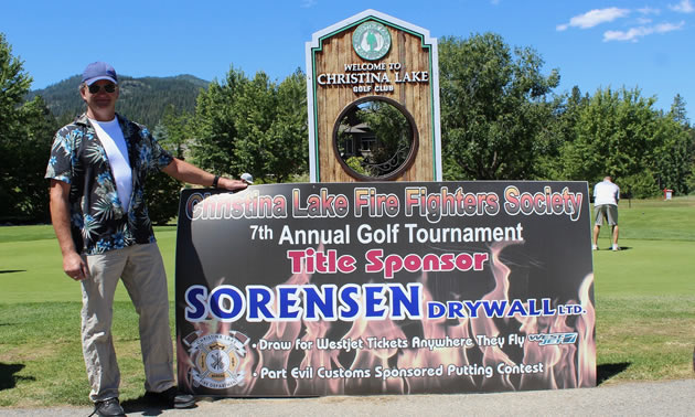 Rob Sorenson poses with last year’s golf tournament banner. 