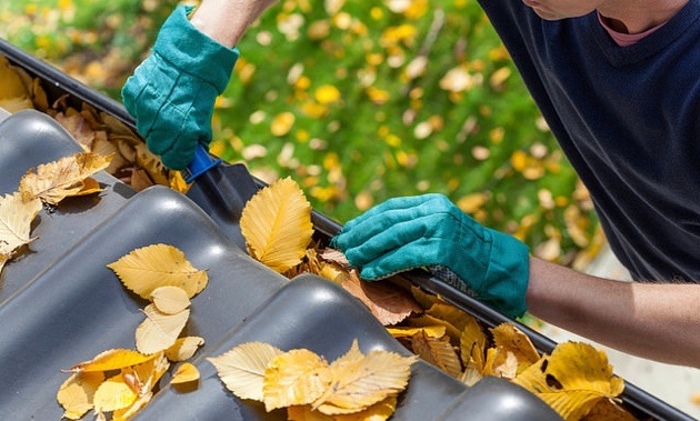 A man cleaning leaves out of the gutter. 