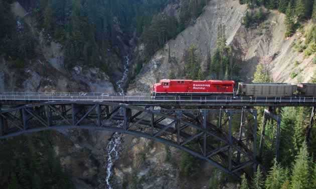 Photo of a coal train driving across a large bridge in the mountains.