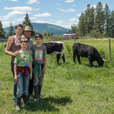 The Bolter family (parents and two kids) stand in a pasture with their beef cows in the background.