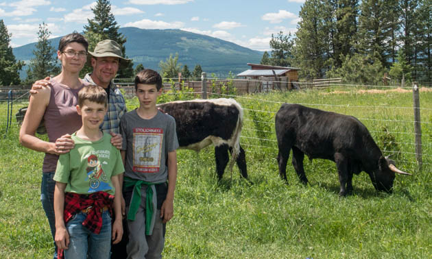 The Bolter family (parents and two kids) stand in a pasture with their beef cows in the background.