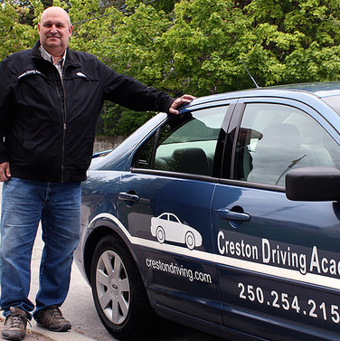 Bill Doeleman, owner and instructor at Creston Driving Academy, is standing next to one of the academy cars.