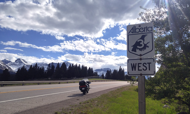 Picture of Highway 3 Alberta sign, with motorcycle parked along shoulder of road. 