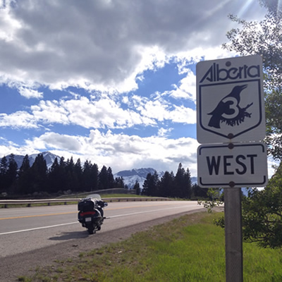 Picture of Highway 3 Alberta sign, with motorcycle parked along shoulder of road. 