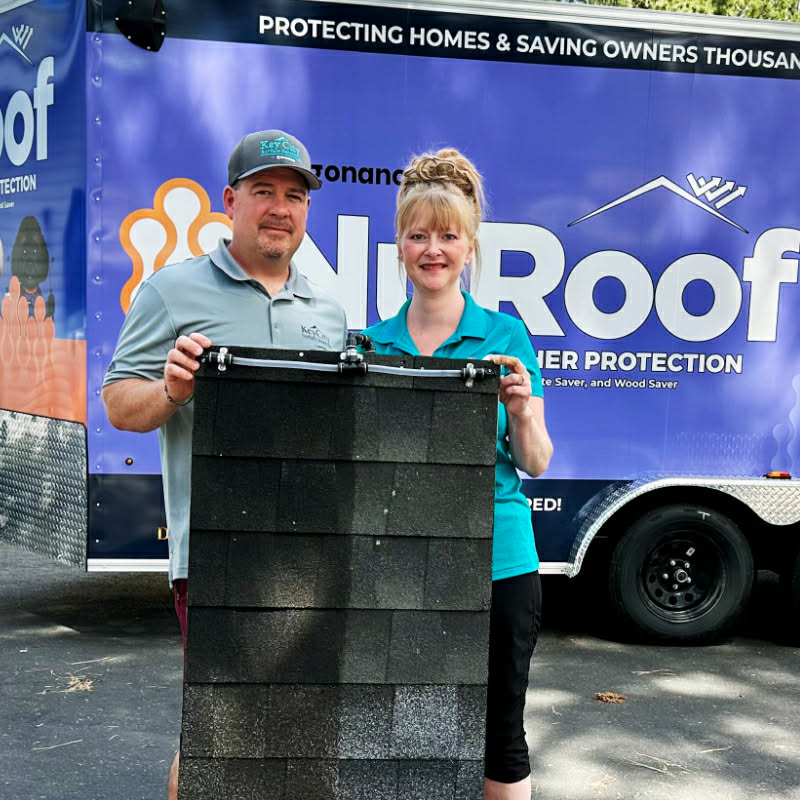 Jeff and Crystal Dyck standing in front of the NuRoof truck holding a sign that says Key City Surface Solutions saved us thousands.