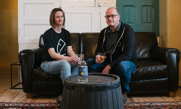 Owners of Fernie Distillers sitting beside a table with a bottle on it