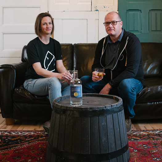 Owners of Fernie Distillers sitting beside a table with a bottle on it