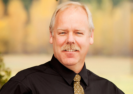 Photo of a guy with a moustache in a black shirt and tie. 