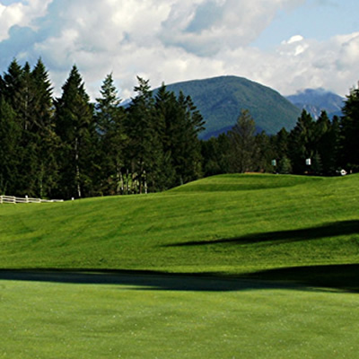Golfer taking a swing along a long fairway, with large mountains in background. 