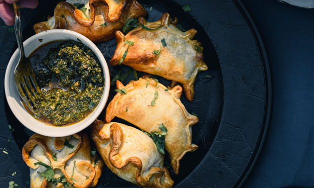 Tray of differently-shaped empanadas, with bowl of dip in centre of plate. 