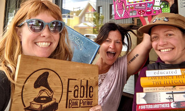 3 female owners of Fable Book Parlour smiling into camera, holding books and sign. 