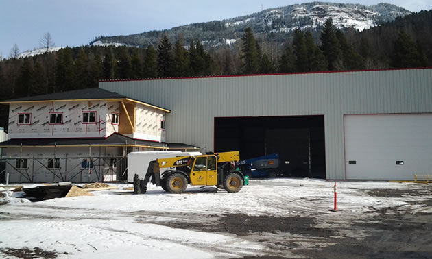 A yellow piece equipment in front of a large shop with the mountains in the background. 