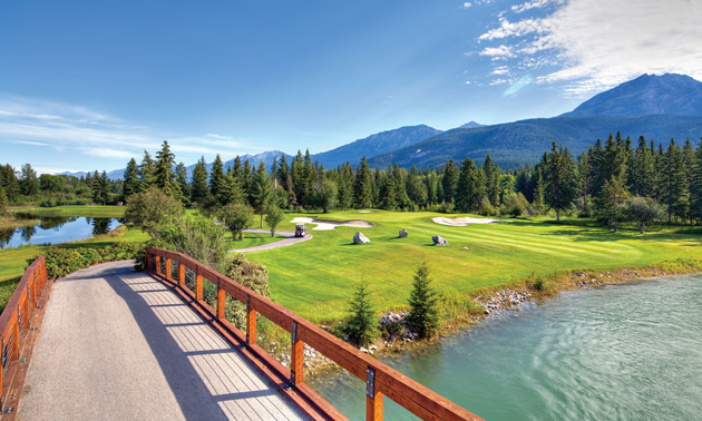 Wooden bridge over waterway, with golf course in the background. 