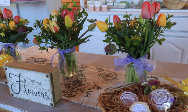 Floral arrangements sitting on counter with basket of handmade soaps. 